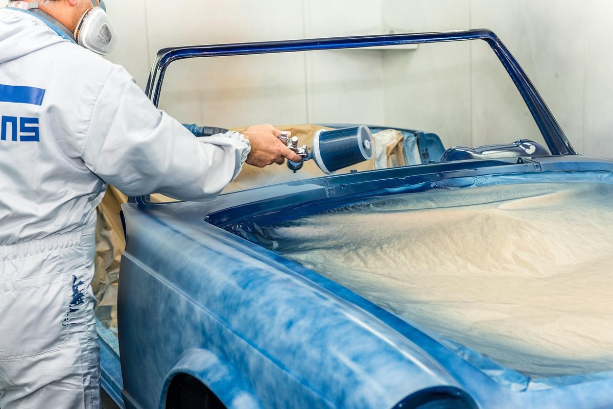 Painter spraying a car in an auto body paint booth (Florida auto body shop insurance)